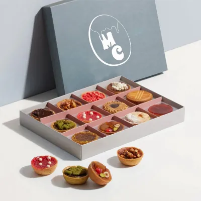 Grey bakery display box with compartments holding assorted small pastries