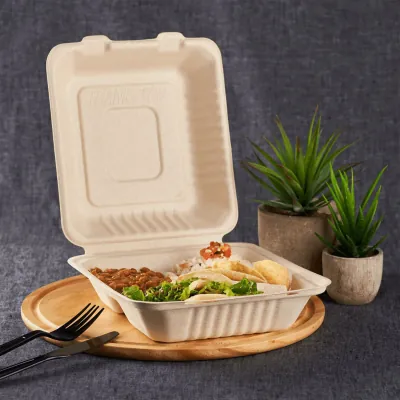 Moulded fibre clamshell open on a wooden board holding a hot meal