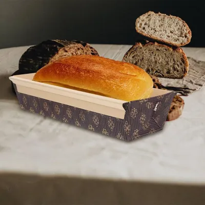 Baked loaf sitting in a patterned paper bake-in loaf case beside artisan sourdough