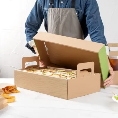 Corrugated catering tray with hand holes and a lid being carried by a member of catering staff
