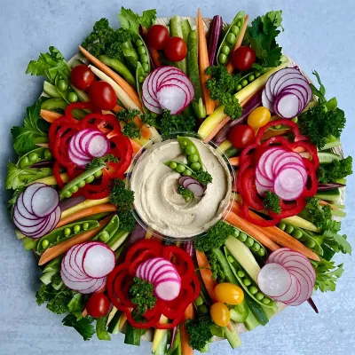 Round crudité arrangement of radishes, peas and carrots around a central dip