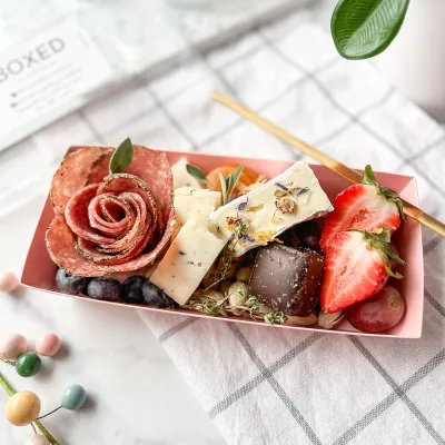 Pink mini charcuterie tray holding rolled salami, cheese and fresh berries
