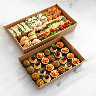 Two kraft rigid catering platters holding sandwiches and canapés