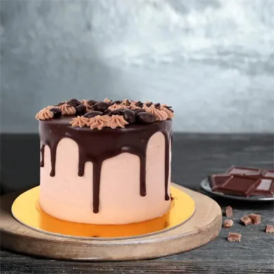 Chocolate drip cake sitting on a gold round cake board