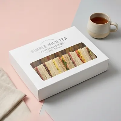 White tea sandwich box with a window showing a row of triangular finger sandwiches